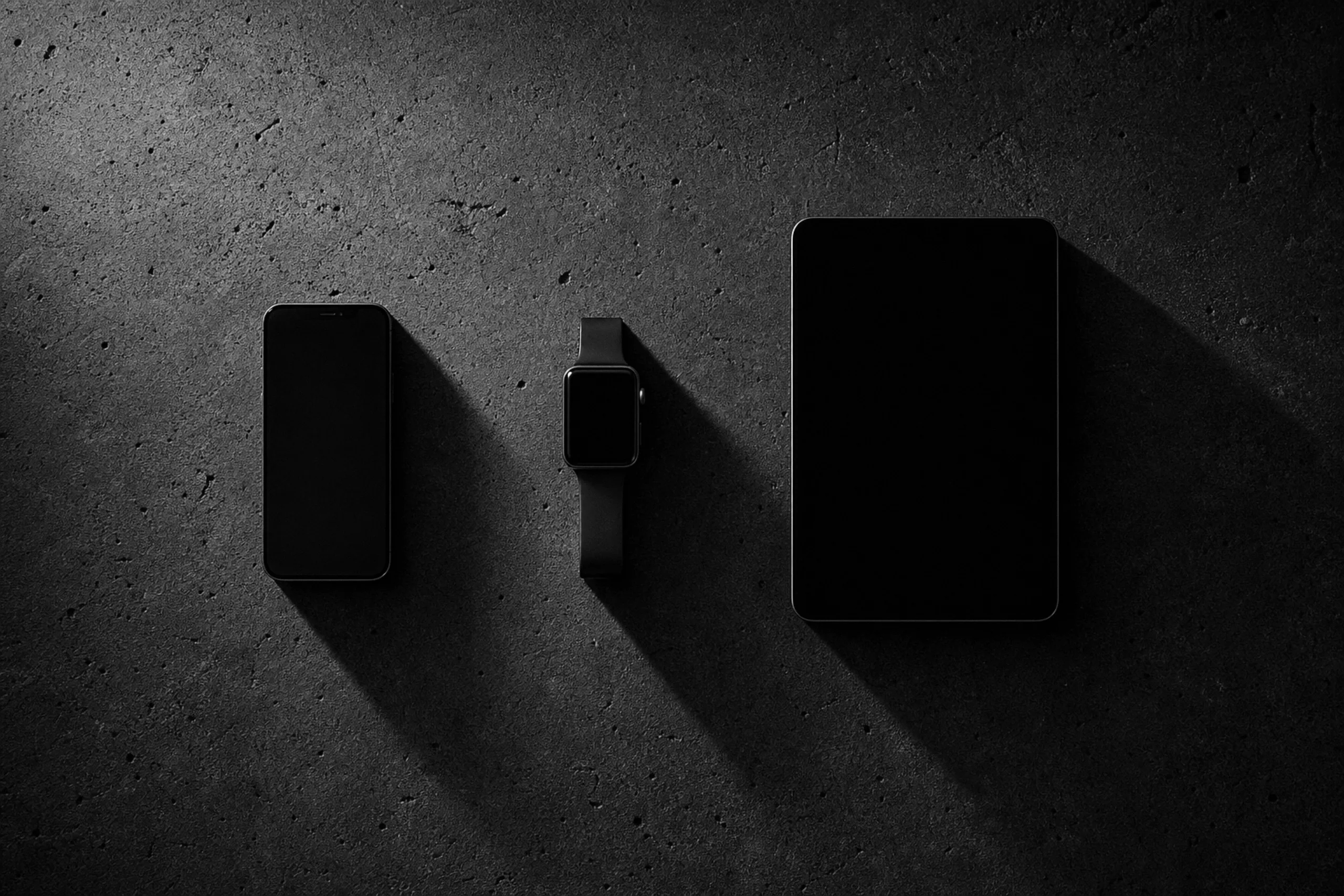 A phone, a watch, and a tablet laid out in a precise row on dark concrete